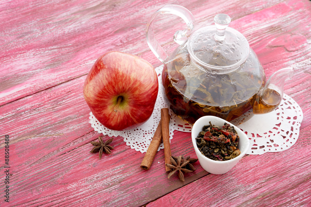 Ripe apple, cinnamon and fruit drink in glass teapot on wooden