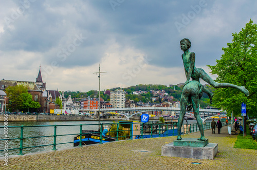 View over riverside of meuse in city of liege with statue of boy jumping over another boy.