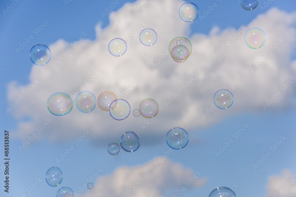 A bunch of colorful soap bubbles flying up into the blue, cloudy sky