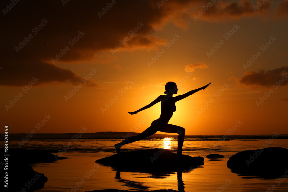Silhouette of woman practicing yoga during sunset at the seaside