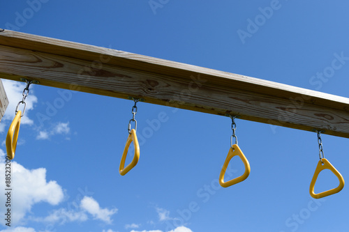 Photography Monkey bar rings hanging from wooden playset with blue sky in background