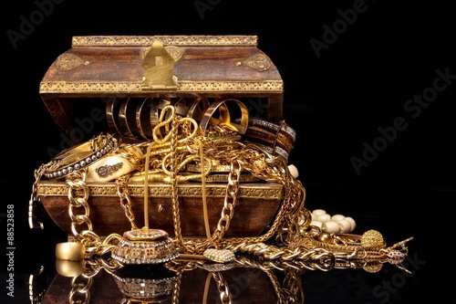 Old brown wooden chest with various golden jewelry, against black background.