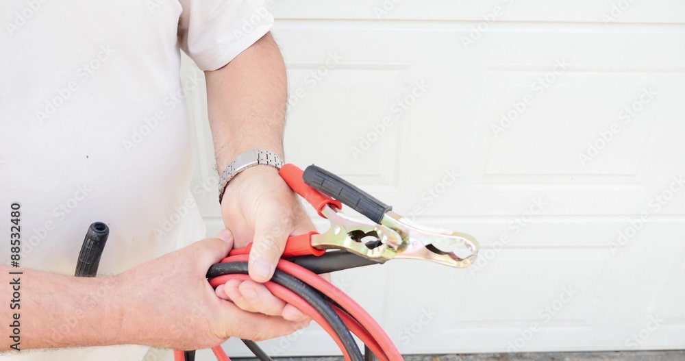 A man in emergency unfolding the booster cables to connect them to the car battery... A man in emergency unfolding the booster cables to connect them to the car battery...