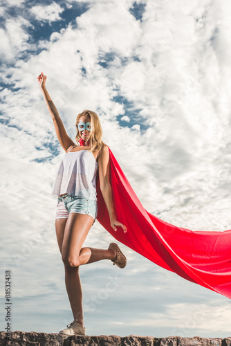 Young woman posing as superhero over blue sky