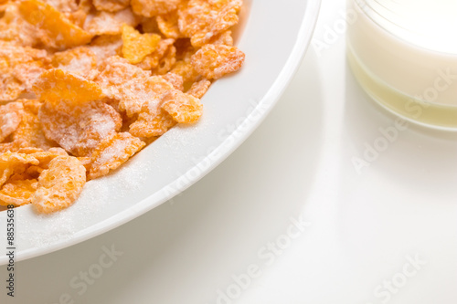 Corn Flakes auf einem Teller und Milch in einer Flasche vor weißem Hintergrund
