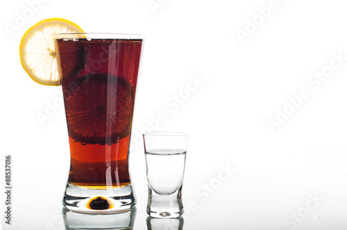 Glass of cola with sliced lemon and shot of vodka