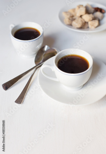 Two cups of coffee on the white table with two spoons 