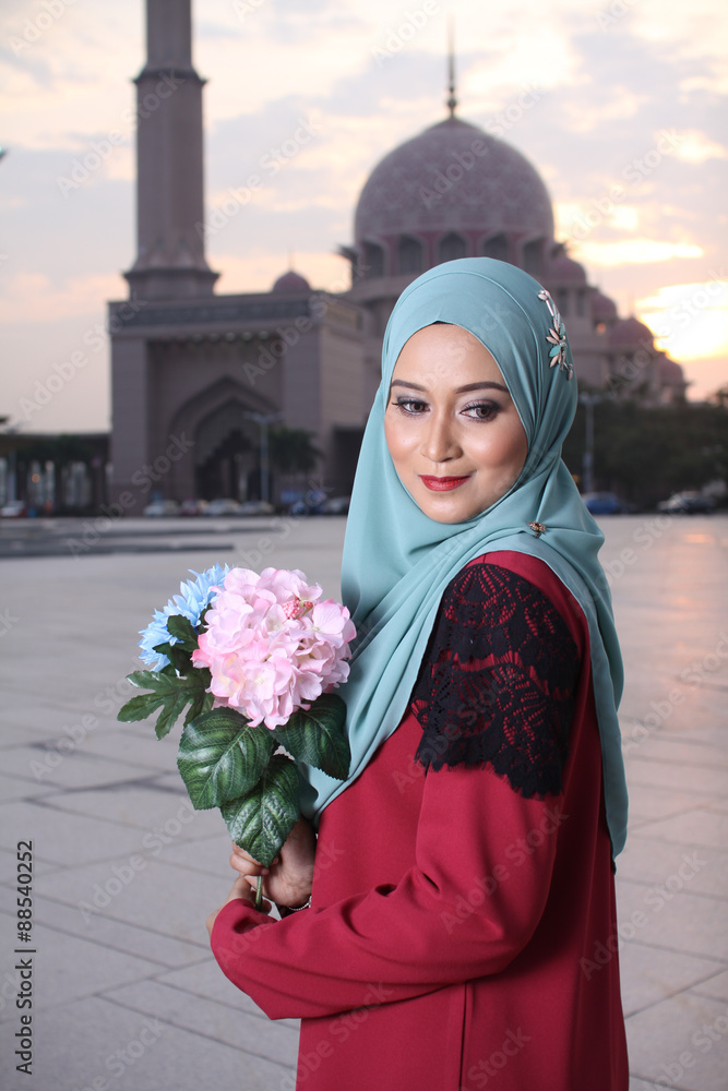 high fashion muslim women holding a flower with mosque background at sunset high fashion muslim women holding a flower with mosque background at sunset