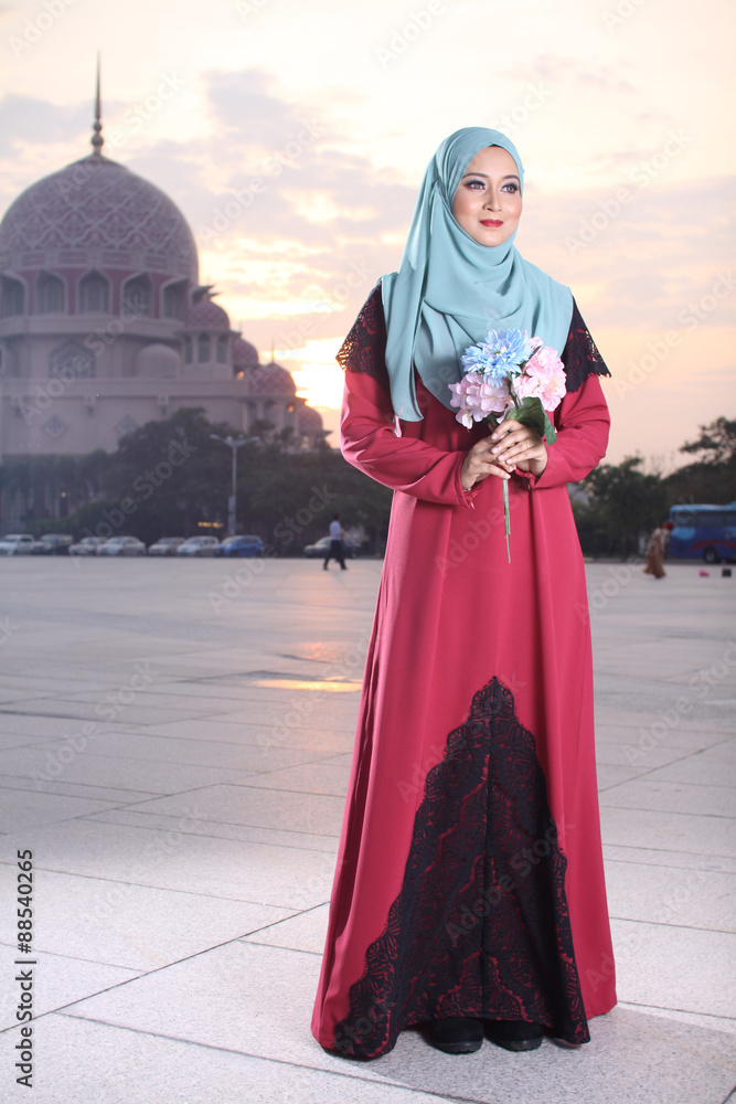 high fashion muslim women holding a flower with mosque background at sunset high fashion muslim women holding a flower with mosque background at sunset