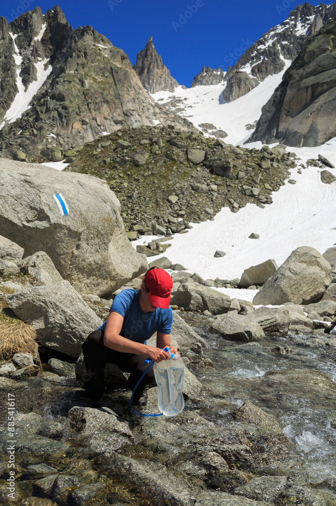 Hiker woman taking water in river in the Swiss mountains after hiking. Enjoying outdoors summer trekking vacation.