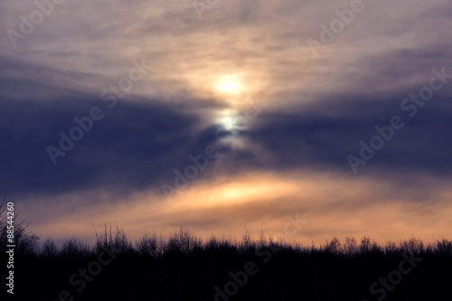 Winter sunset over forest with clouds on evening sky