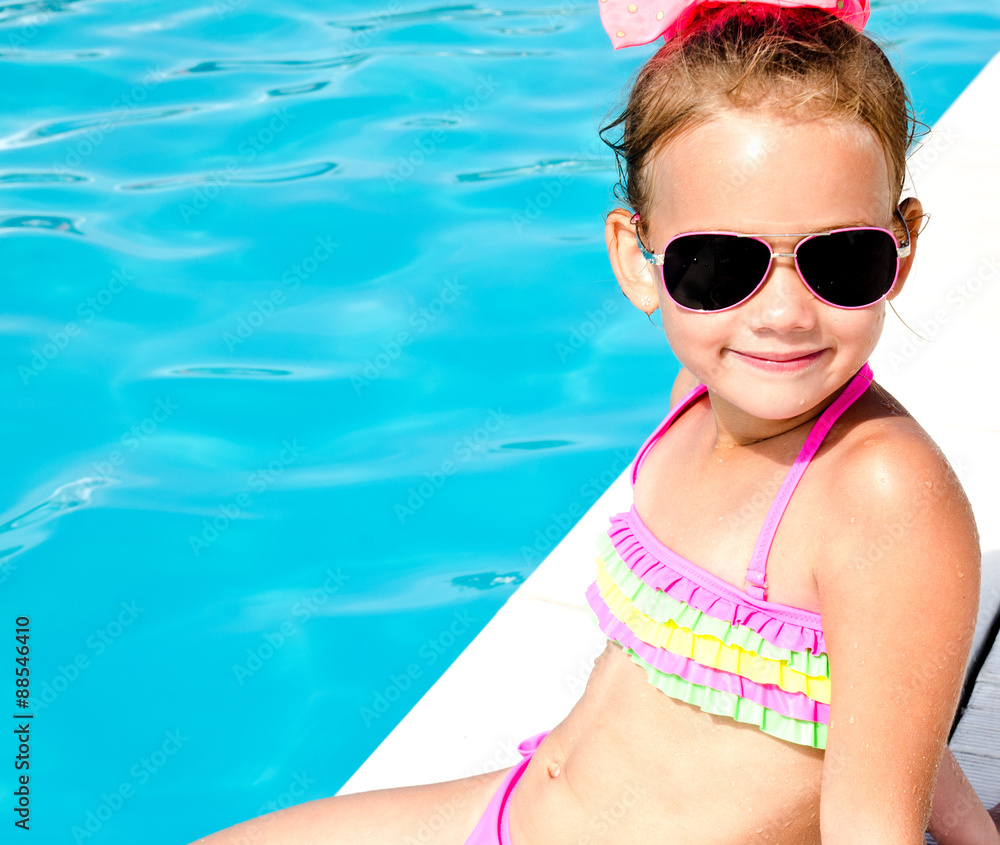 Smiling little girl sitting near swimming pool