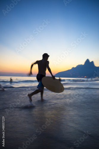 Sunset silhouette of carioca Brazilian running with skimboard on Ipanema Beach Rio de Janeiro Brazil  photo