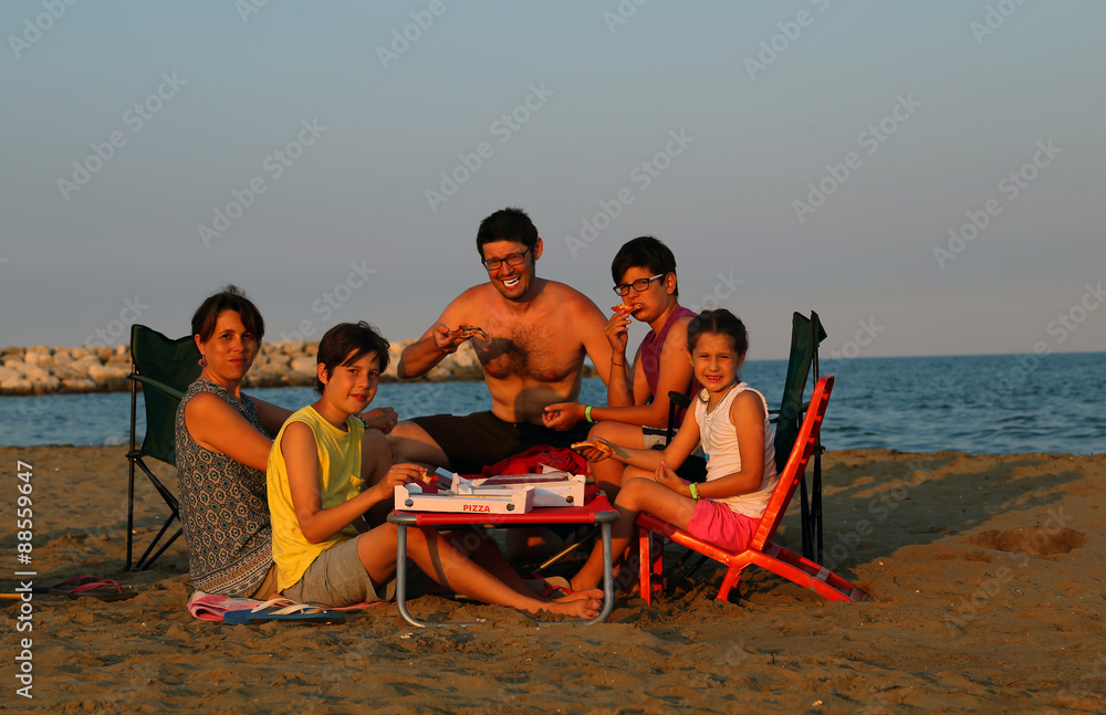 happy family of five eats pizza on the beach