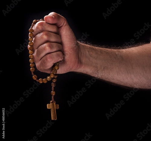 Hand with a chaplet against dark background, religious concept