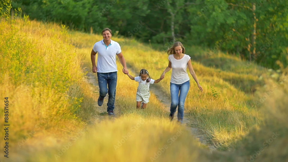 The family (father, mother and daughter) run on the way by forest background The family (father, mother and daughter) run on the way by forest background