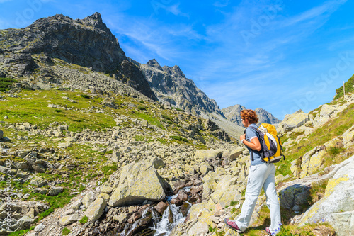 Young woman backpacker looking at waterfall in summer landscape of High Tatra Mountains, Slovakia