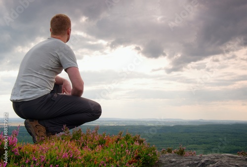 Hiker in squatting position on a rock in heather bushes, enjoy the cloudy scenery