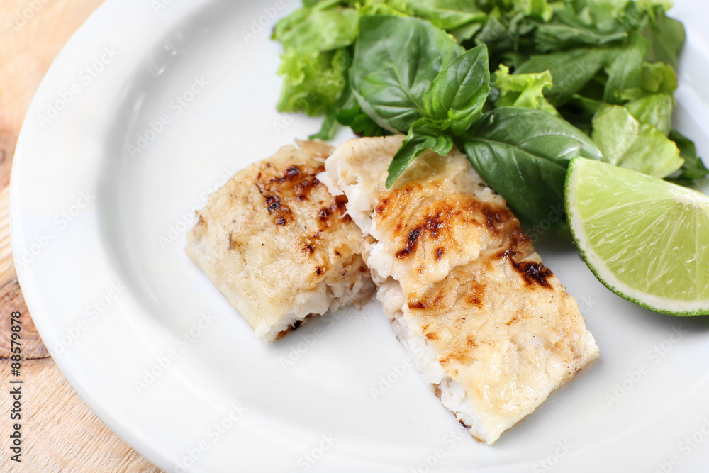 Dish of fish fillet with greens and lime on plate close up Dish of fish fillet with greens and lime on plate close up