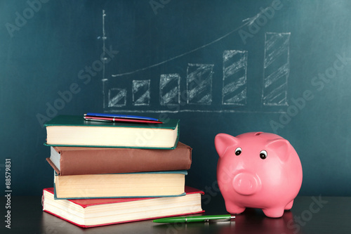 Piggy bank with books on blackboard background