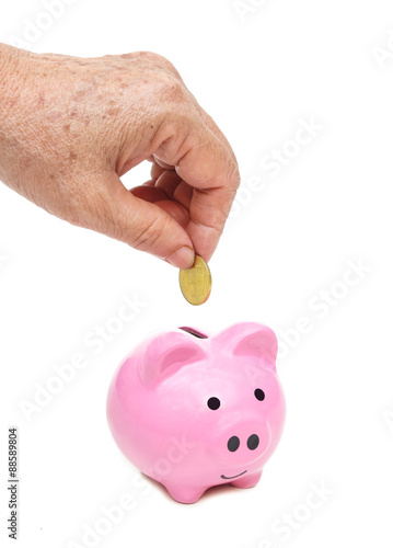 old female elderly hand putting a golden coin into a saving piggy bank - saving money for retirement concept