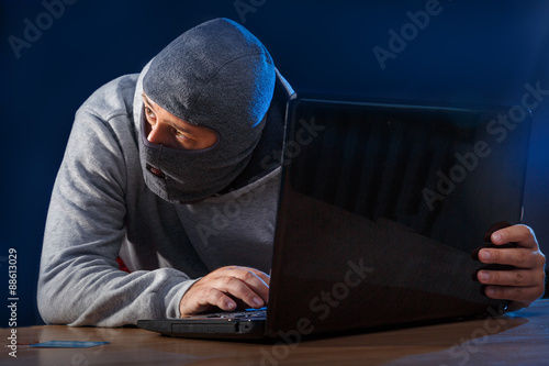 Cyber criminal hacking into a computer. looking over his shoulder.