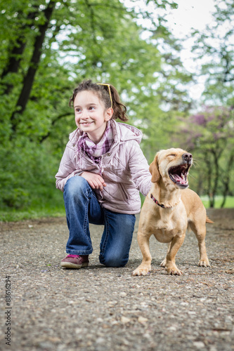 Photo of a little girl kneeling in the park with a dog