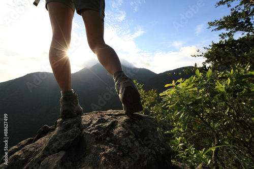 young woman hiker legs on sunrise mountain peak rock
