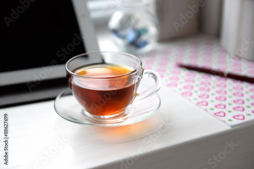 Cup of tea near PC tablet, notebook on windowsill, close-up. Working place concept