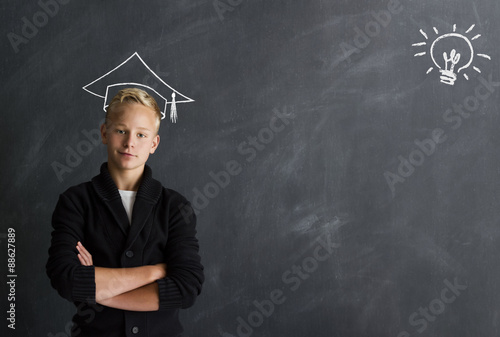 Intelligenter Jungen mit Doktorhut vor Tafel