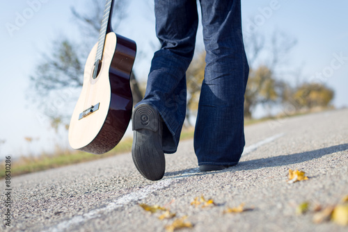 Legs walking away with guitar aside on empty country road