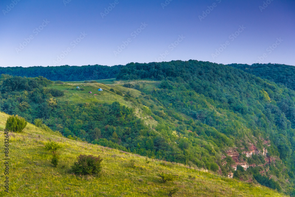 Beautiful summer mountain landscape. Tourist tents on meadow near forest. Beautiful summer mountain landscape. Tourist tents on meadow near forest.