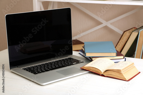 Laptop with books on table in room