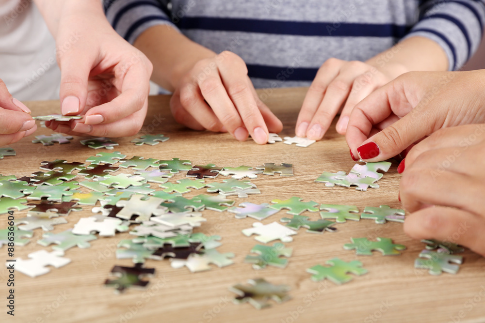 Fototapeta premium Female hands assembling puzzle on wooden table, closeup