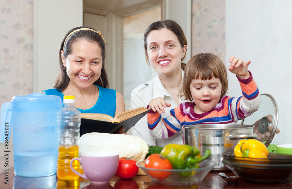 Mature woman and adult daughter with baby girl cook vegetables