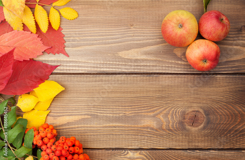 Autumn leaves  rowan berries and apples over wood background