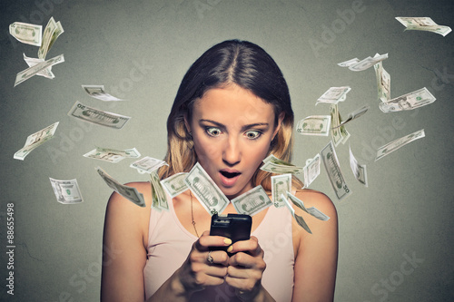Billede på lærred Shocked woman using smartphone dollar bills flying away from screen