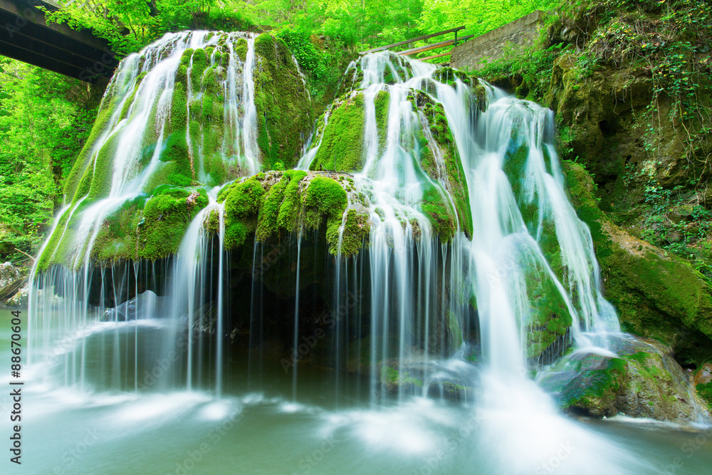 Fototapeta premium Cascade falls over mossy rocks in forest