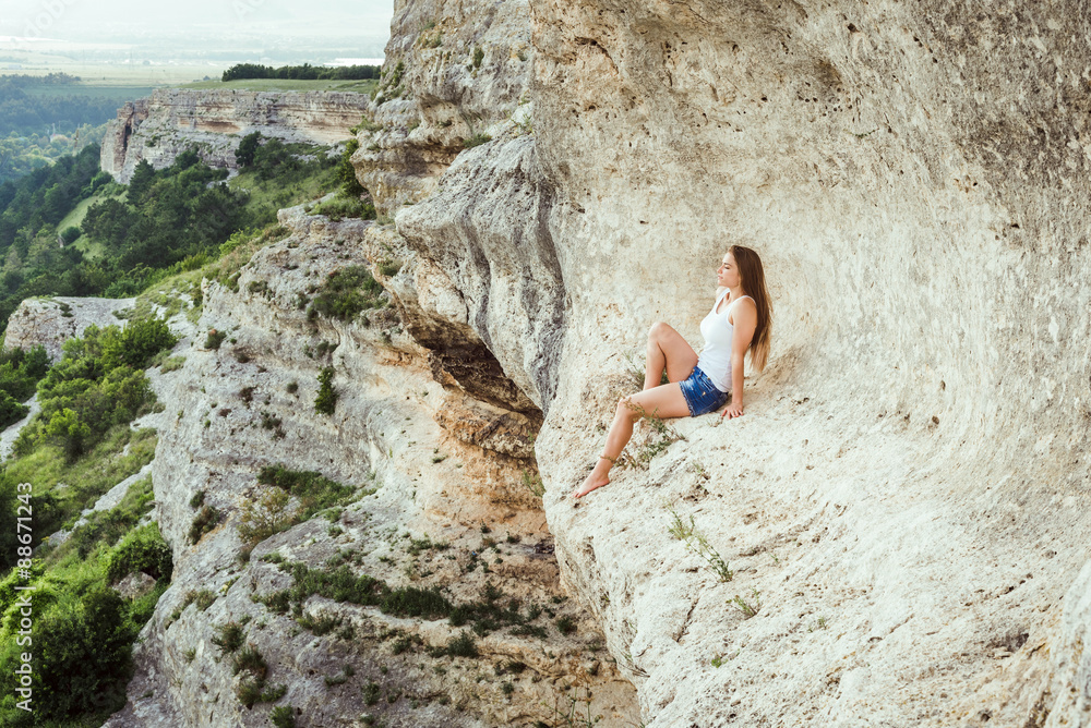 young caucasian female sitting on a cliff and looking at view in crimea mountains