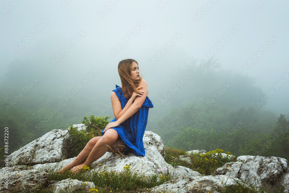 young caucasian female posing in blue dress in mountains in foggy weather young caucasian female posing in blue dress in mountains in foggy weather