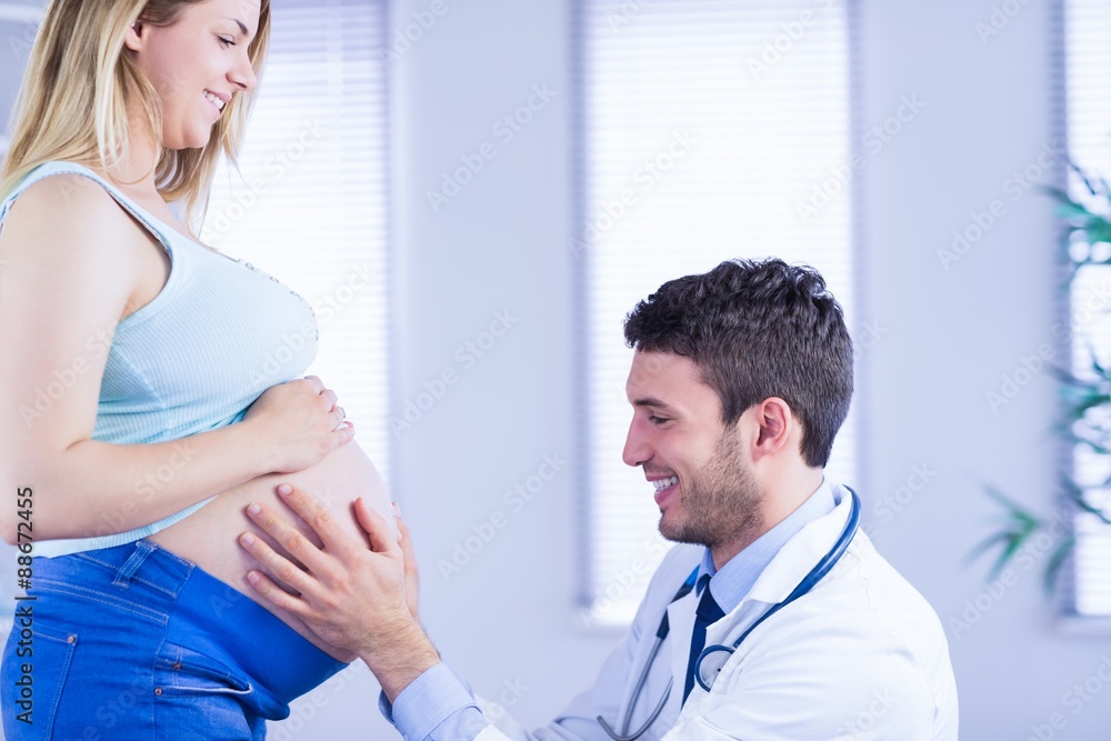 Smiling doctor checking stomach of standing pregnant patient Smiling doctor checking stomach of standing pregnant patient