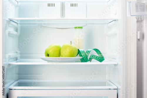 Two apples with measuring tape and glass bottle in refrigerator