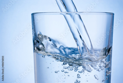 Close-up pouring water into glass on blue background
