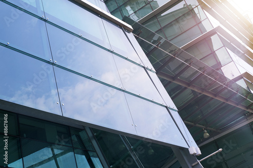 Modern facade of glass and steel with window reflecting sky and clouds.