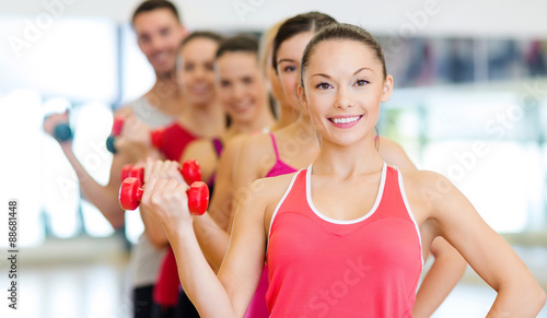 group of smiling people with dumbbells in the gym