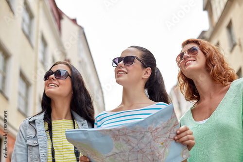 smiling teenage girls with map and camera outdoors