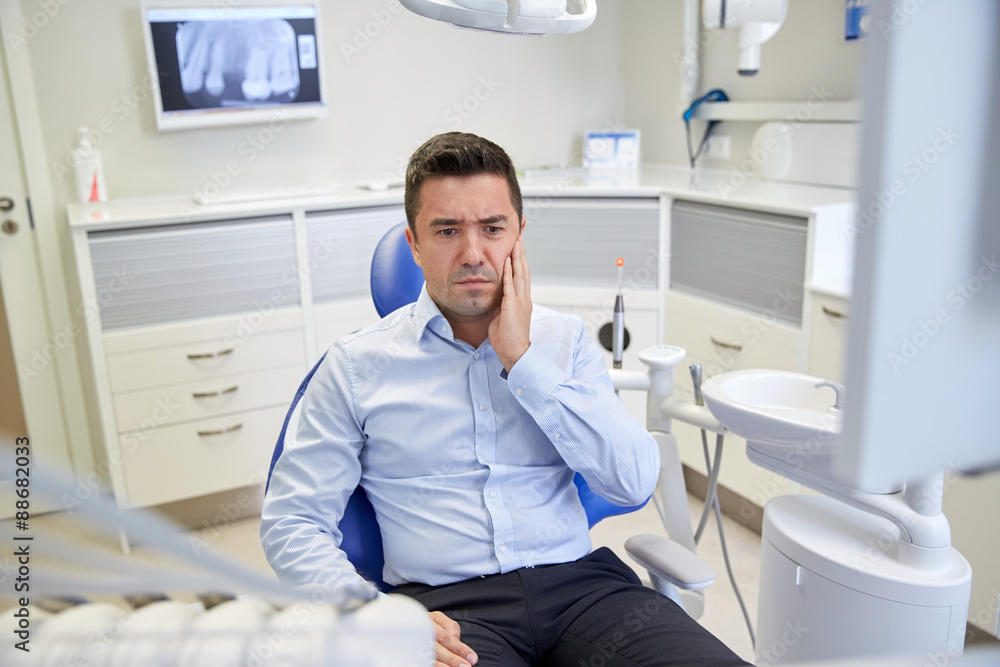man having toothache and sitting on dental chair