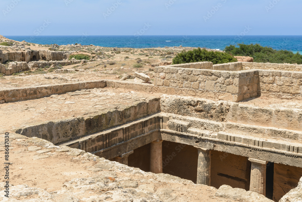 Looking down into a chamber of an ancient carved stone burial tomb at an archaeological site in Paphos, Cyprus with the blue Mediterranean Sea in the background. Looking down into a chamber of an ancient carved stone burial tomb at an archaeological site in Paphos, Cyprus with the blue Mediterranean Sea in the background.