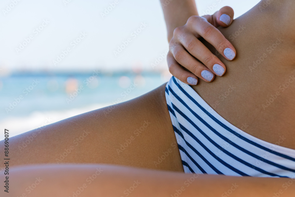 Female slim tanned body in a swimsuit on the beach close-up on a