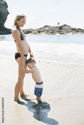 Woman in a bikini playing with her son on a sandy beach by the ocean. photo